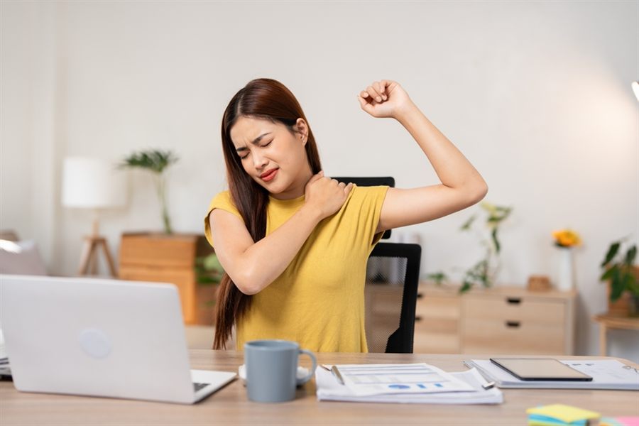 A woman at a desk holding her neck and shoulder in discomfort